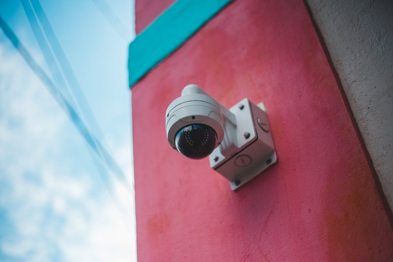 services-03 A surveillance camera mounted on a vibrant pink and teal wall outdoors.