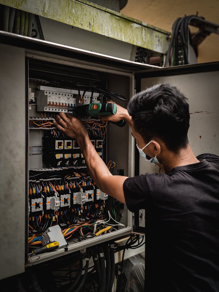 who-we-are Technician working on circuit breaker panel, adjusting electrical wires indoors.